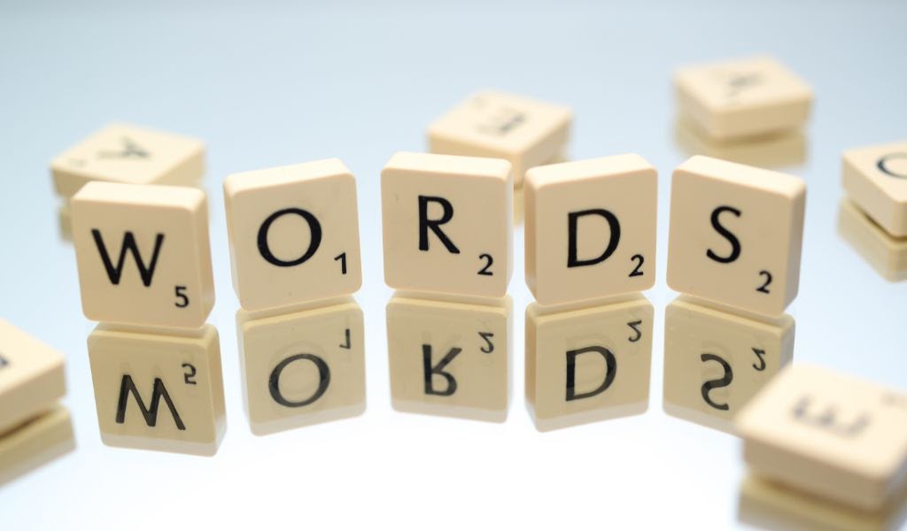 Jednotlivá písmenka W, O, R, D a S ze hry Scrabble volně postavená vedle sebe na zrcadlové ploše.
